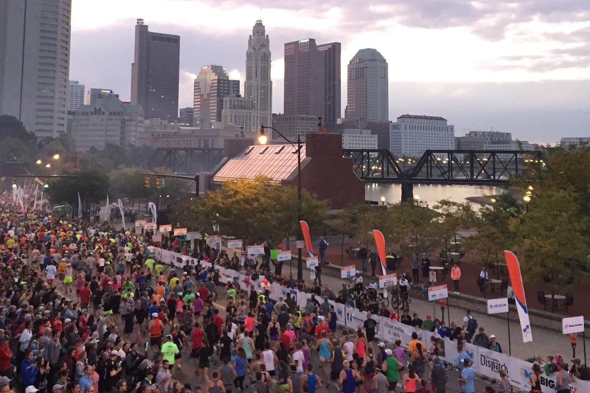Runners packing a downtown Columbus marathon course near the skyline