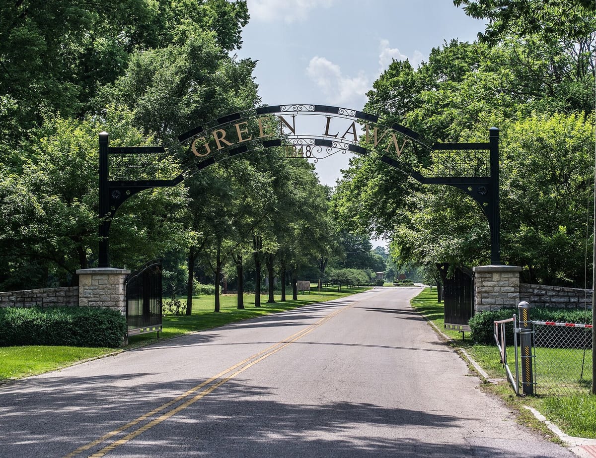 Iron arch gateway spelling Green Lawn over a tree-lined road into Green Lawn Cemetery in Columbus