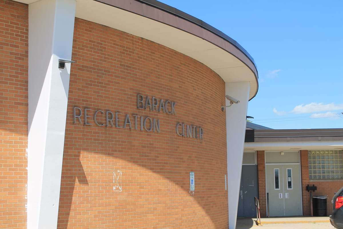 Curved tan brick facade of Barack Recreation Center with raised letters and glass entry doors on a sunny day