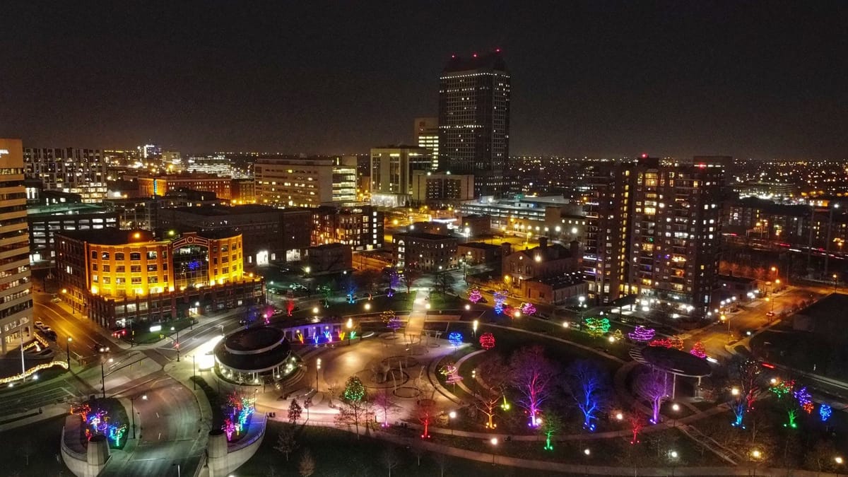 Aerial night view of Bicentennial Park in Downtown Columbus with trees wrapped in colored lights around the fountain plaza