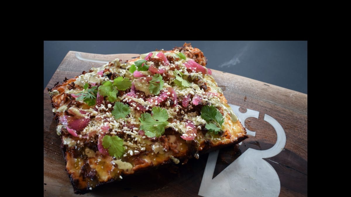 Square Detroit-style Black Pony Pizza slice with pickled onion, cilantro, and BP logo board