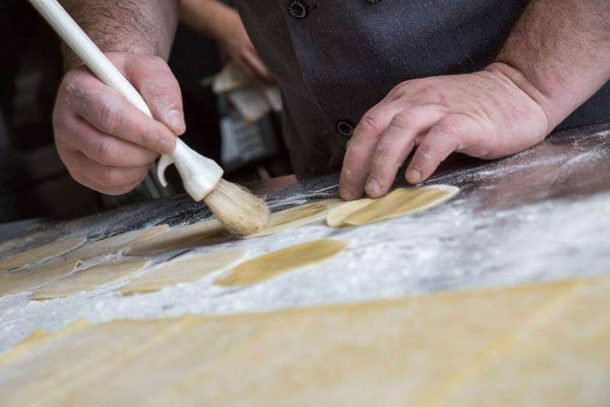 Hands brushing fresh pasta rounds with flour for Sunday Gravy Italian kitchen concept