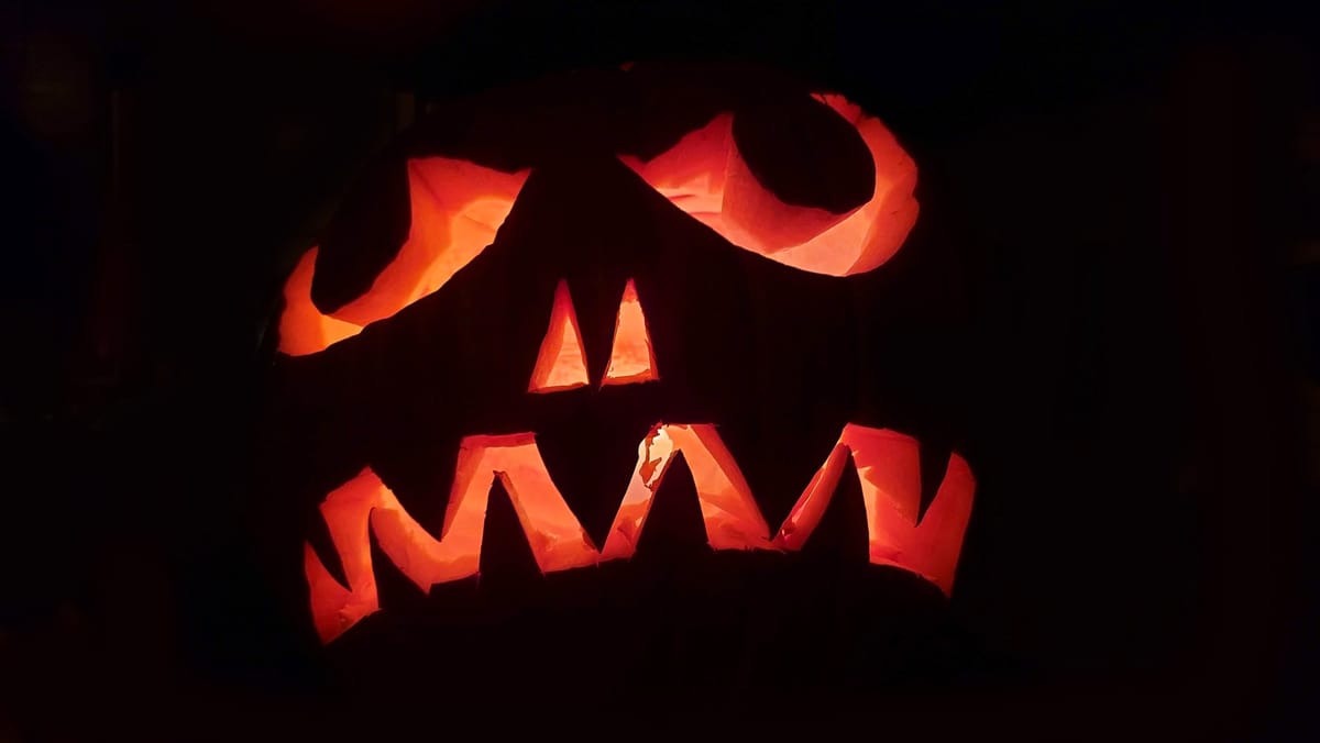 A carved jack-o'-lantern with angled eyes and jagged teeth glowing orange in the dark