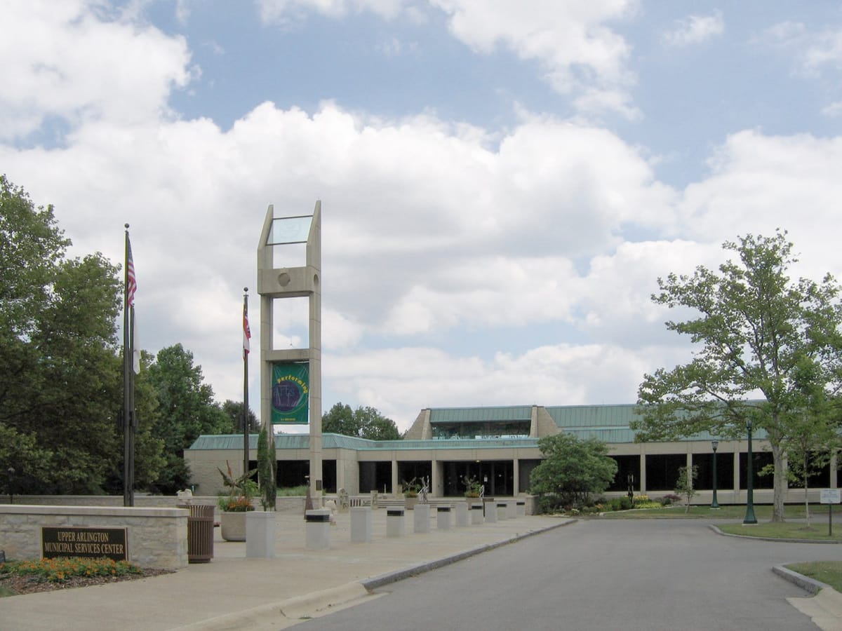 Upper Arlington Municipal Services Center, a low stone building with a green roof behind a tall concrete tower, two flagpoles and an entry drive