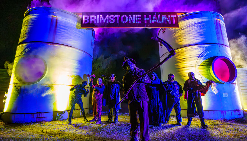 Costumed Brimstone Haunt actors posed under a lit Brimstone Haunt entrance archway at night