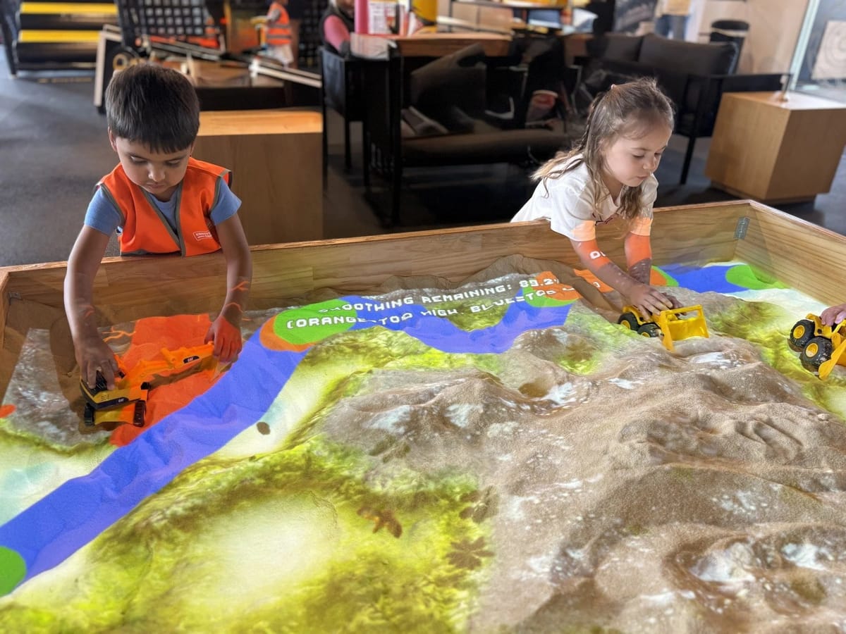 Toddlers at Construction Corner interactive sand table with toy excavators
