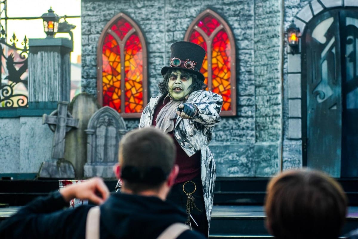 Costumed Halloween Haunt performer in a top hat looming over guests on a gothic Kings Island street set