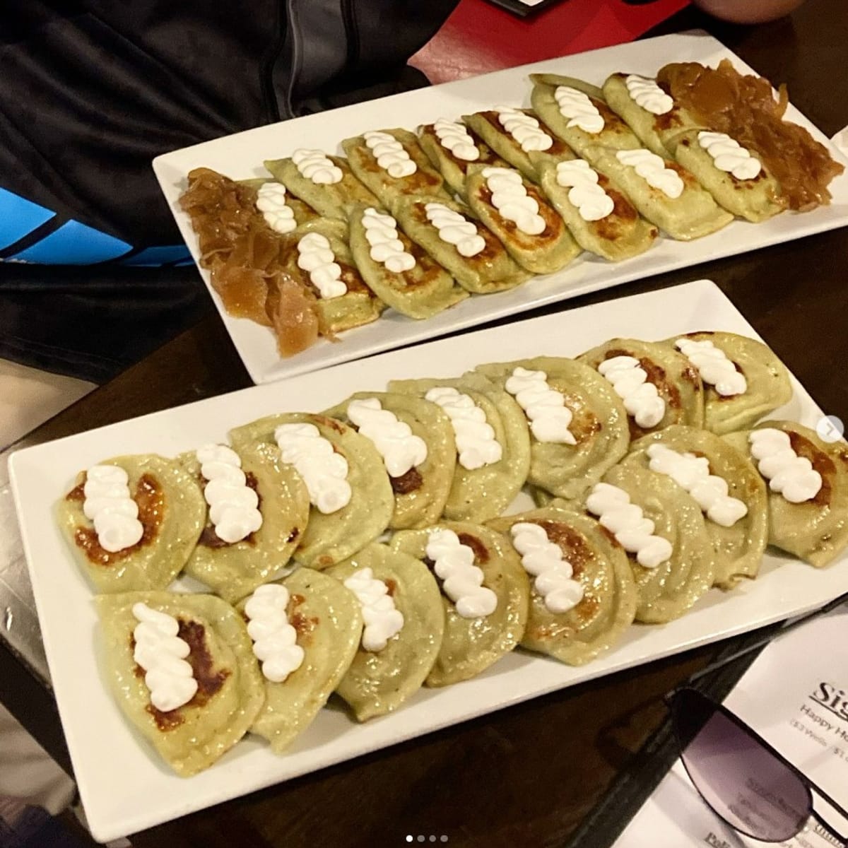 Two platters of Pierogi Mountain pierogies with sour cream and onions
