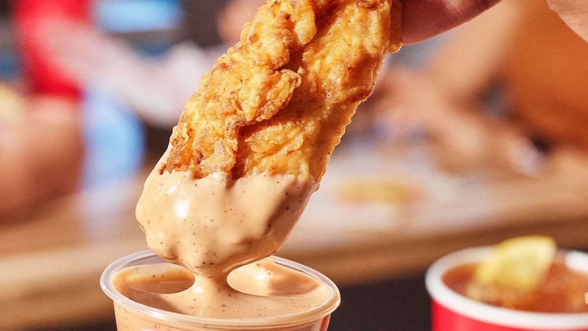 Raising Cane's chicken tender dipped in Cane's sauce