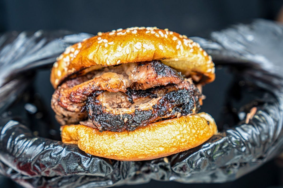 Gloved hands holding a smoked brisket sandwich