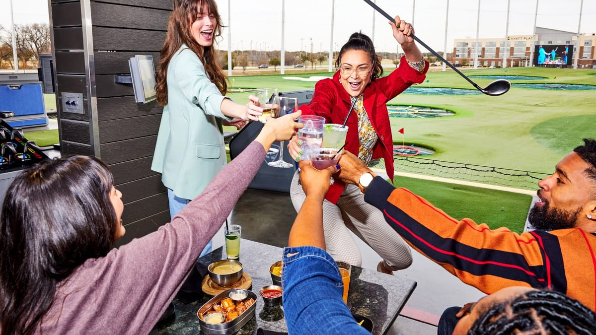 Friends toasting in a Topgolf Columbus bay overlooking the range