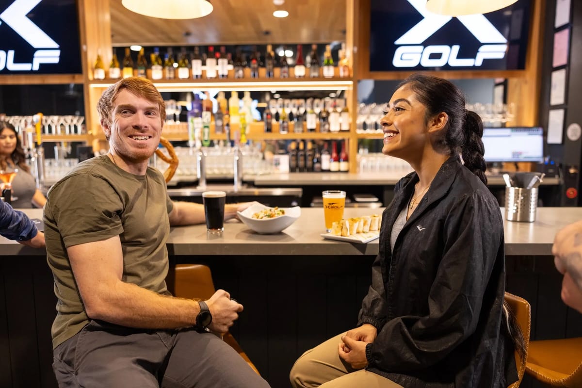 Couple dining at the X-Golf bar with X GOLF screens behind