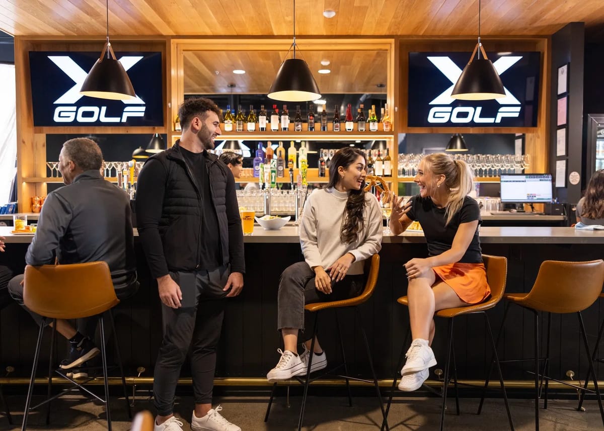 Guests at the bar inside an X-Golf lounge with X GOLF screens